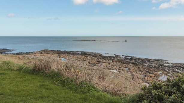 A rocky shoreline with a clear view of the sea and a distant buoy.