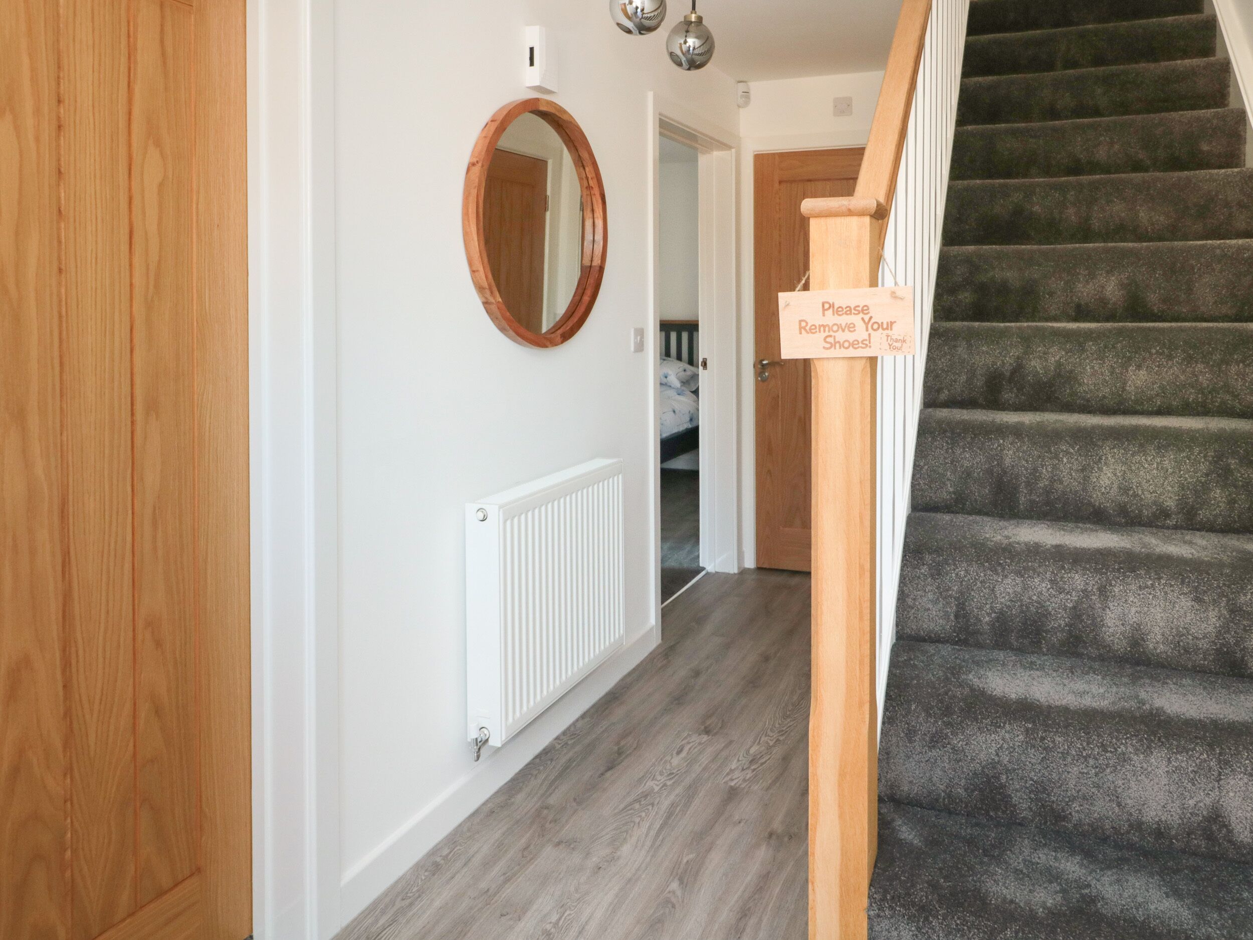 A hallway with a wooden door, a white radiator, a mirror, and a staircase with a sign asking guests to remove their shoes.