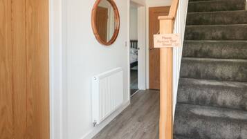 A hallway with a wooden door, a white radiator, a mirror, and a staircase with a sign asking guests to remove their shoes.