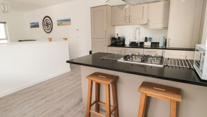A modern kitchen with a black countertop, stainless steel appliances, wooden stools, and light-colored cabinets.