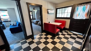 Ein Zimmer mit Schachbrettmuster-Boden, einer roten Sitzecke und Blick auf ein Schlafzimmer mit Bett und Fenster.
