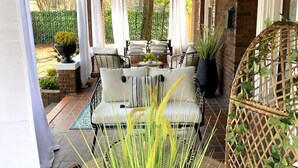 Un patio cubierto con mobiliario exterior, plantas en macetas y una pared de ladrillo.