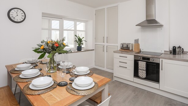 A modern kitchen with white cabinets, a stainless steel range hood, and a built-in oven. - Gwynant - Bull Bay (Amlwch)