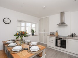 A modern kitchen with white cabinets, a stainless steel range hood, and a built-in oven.