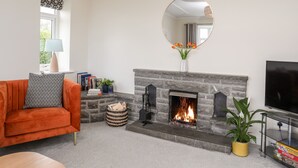 A living room with a fireplace, a sofa, a TV, and a mirror. - Gwynant - Bull Bay (Amlwch)