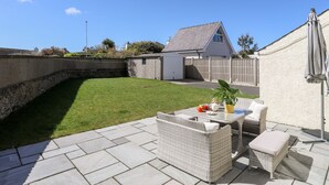 A patio area with a wicker sofa set, a small table with a plant, and a white wall with a window. - Gwynant - Bull Bay (Amlwch)