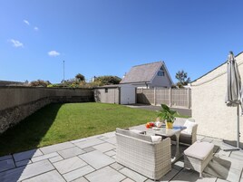 A patio area with a wicker sofa set, a small table with a plant, and a white wall with a window.