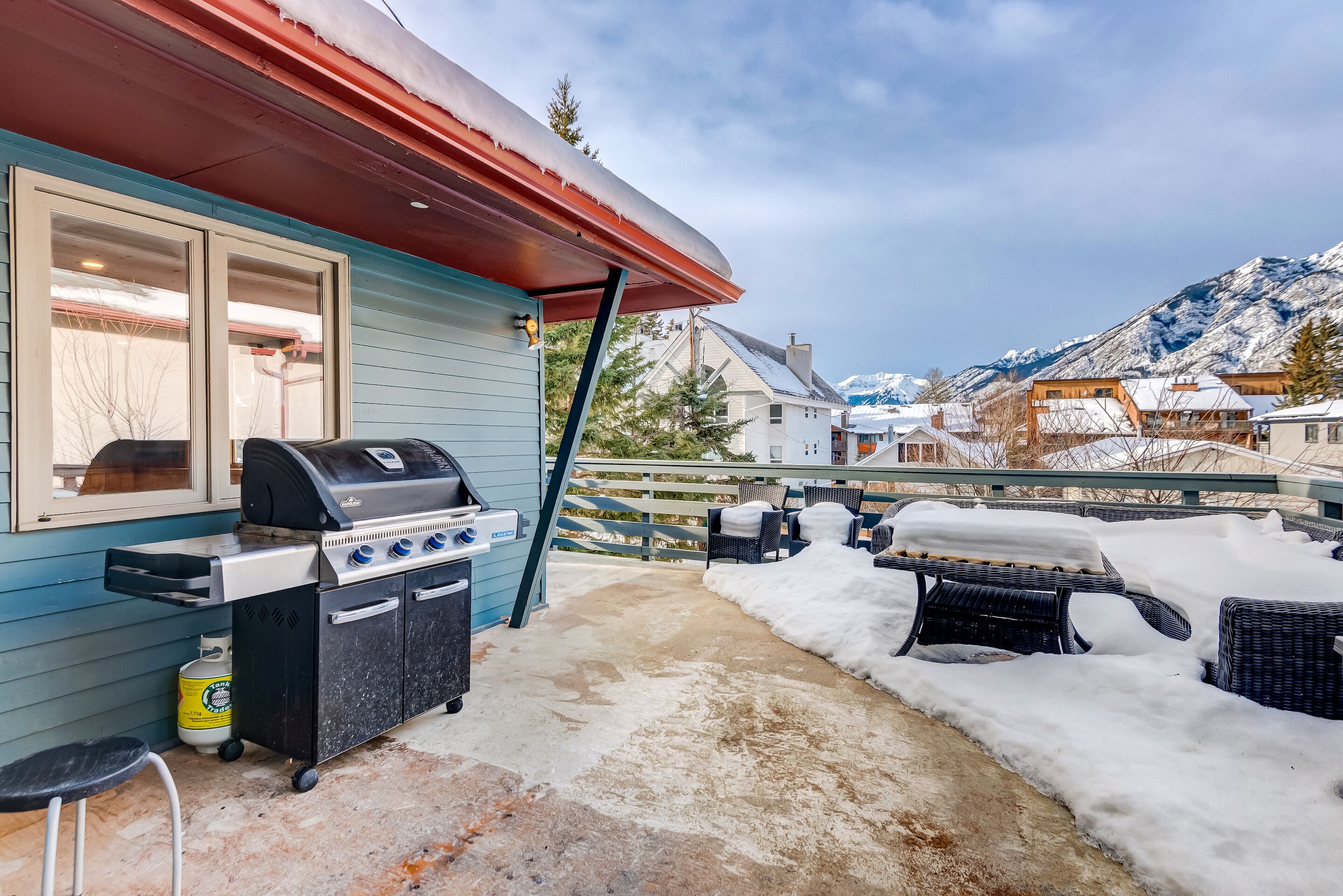 A patio with a barbecue grill, outdoor seating, and a view of snow-covered mountains.