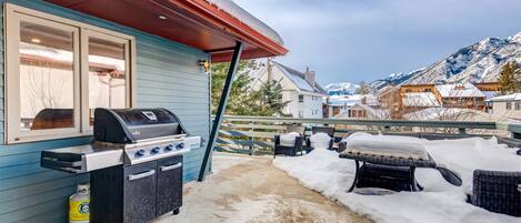 A patio with a barbecue grill, outdoor seating, and a view of snow-covered mountains.