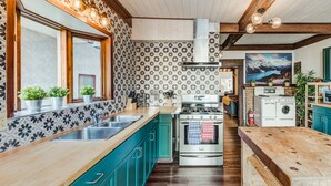 Cucina con piano di lavoro in legno, elettrodomestici in acciaio inossidabile, mobili in verde acqua e un'ampia finestra.