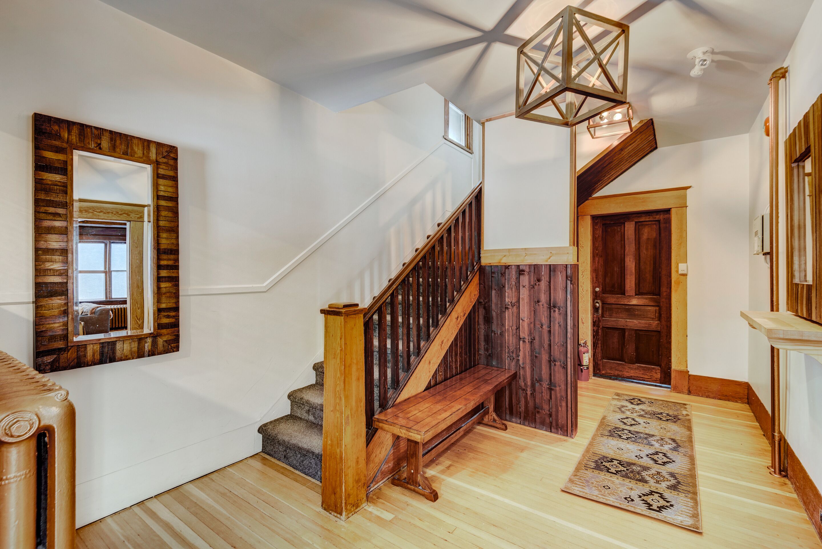 A staircase with wooden railings and a wooden bench, a wooden door, and a patterned rug on a wooden floor.