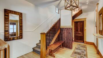 A staircase with wooden railings and a wooden bench, a wooden door, and a patterned rug on a wooden floor.