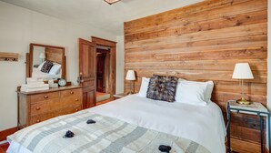 Una camera da letto con testiera in legno, un letto con lenzuola bianche, una cassettiera in legno, uno specchio e due lampade da comodino.