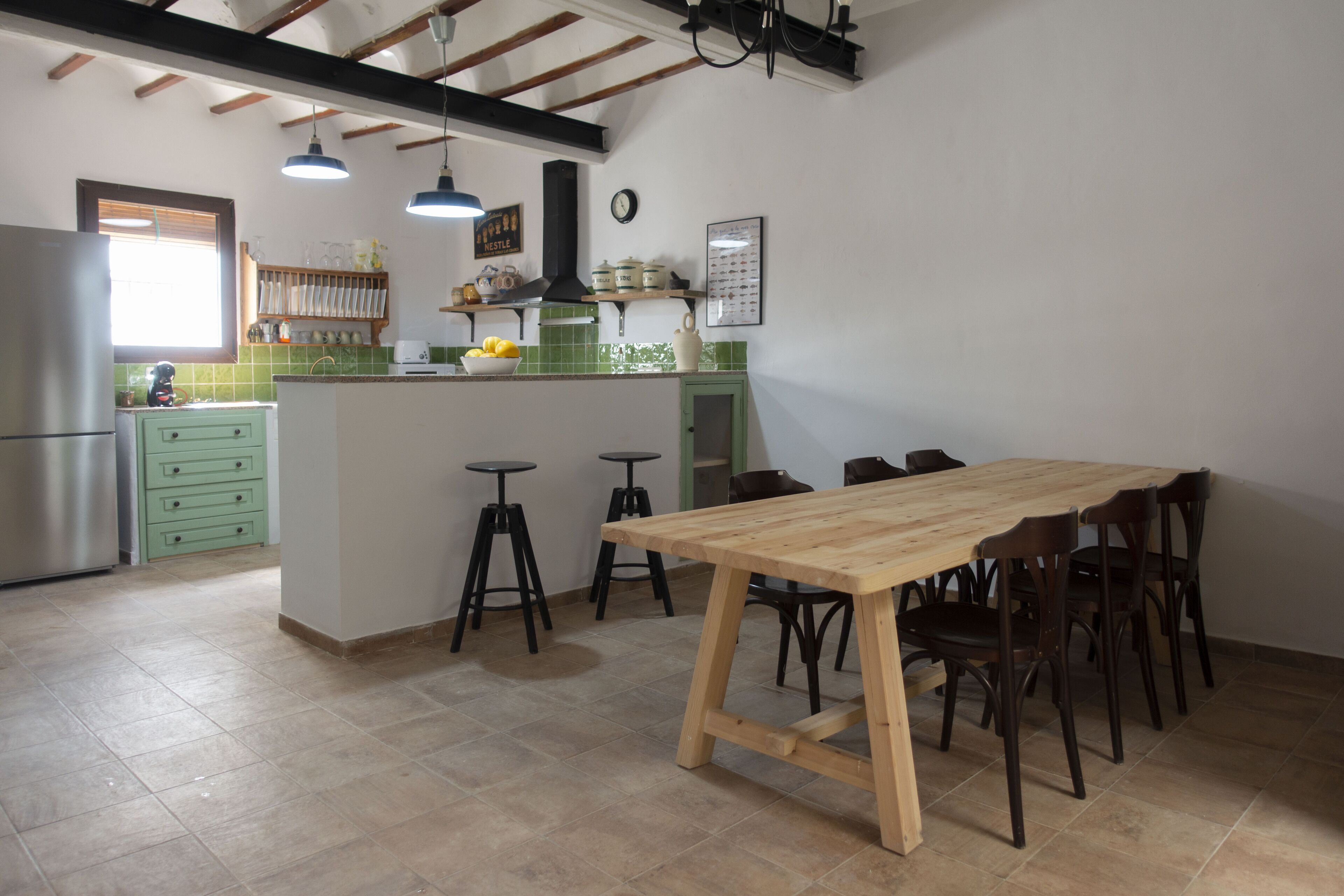 Une cuisine avec une table et des chaises en bois, des armoires vertes et un réfrigérateur en acier inoxydable.