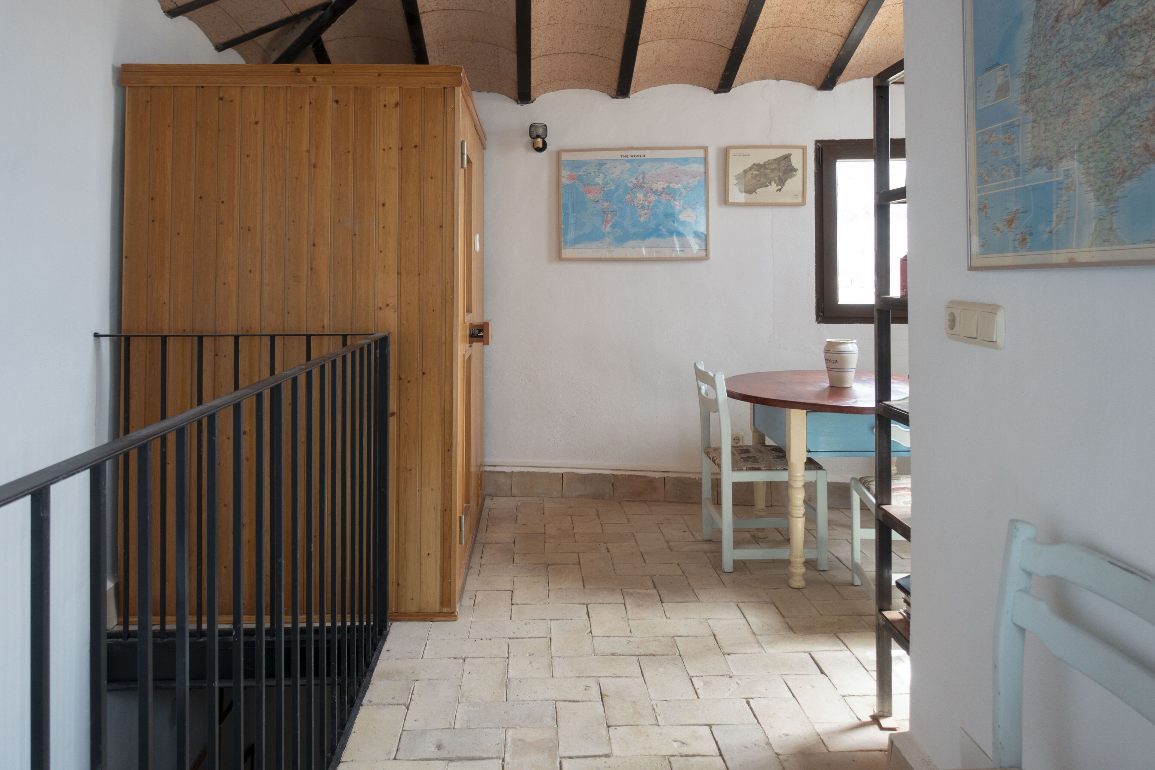 Una habitación con puerta de madera, una mesa pequeña con sillas, un mapa en la pared y suelo de baldosas.