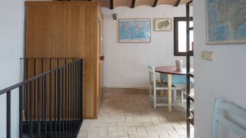 Una habitación con puerta de madera, una mesa pequeña con sillas, un mapa en la pared y suelo de baldosas.