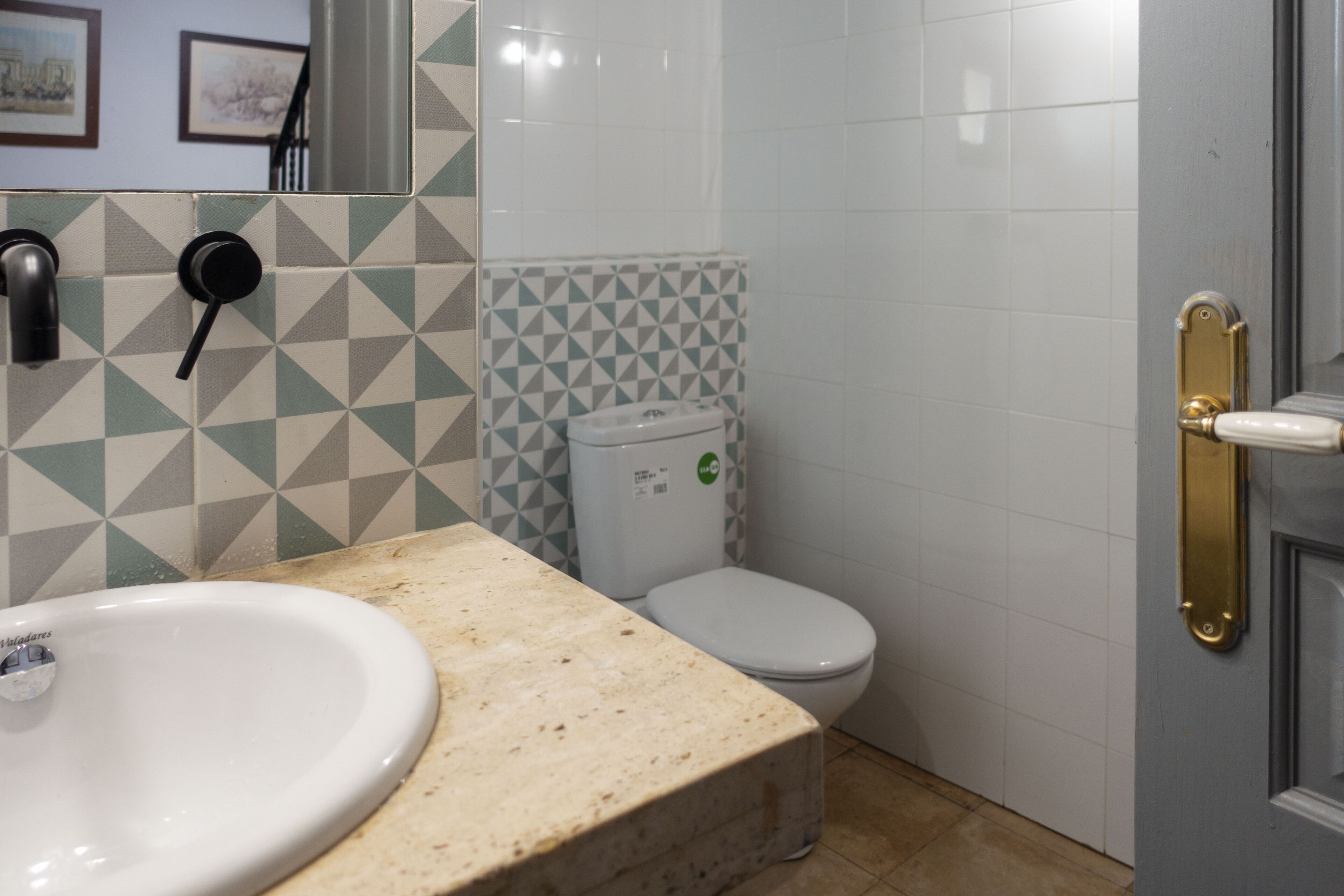 Un baño con lavamanos, inodoro y una puerta con pomo de latón.