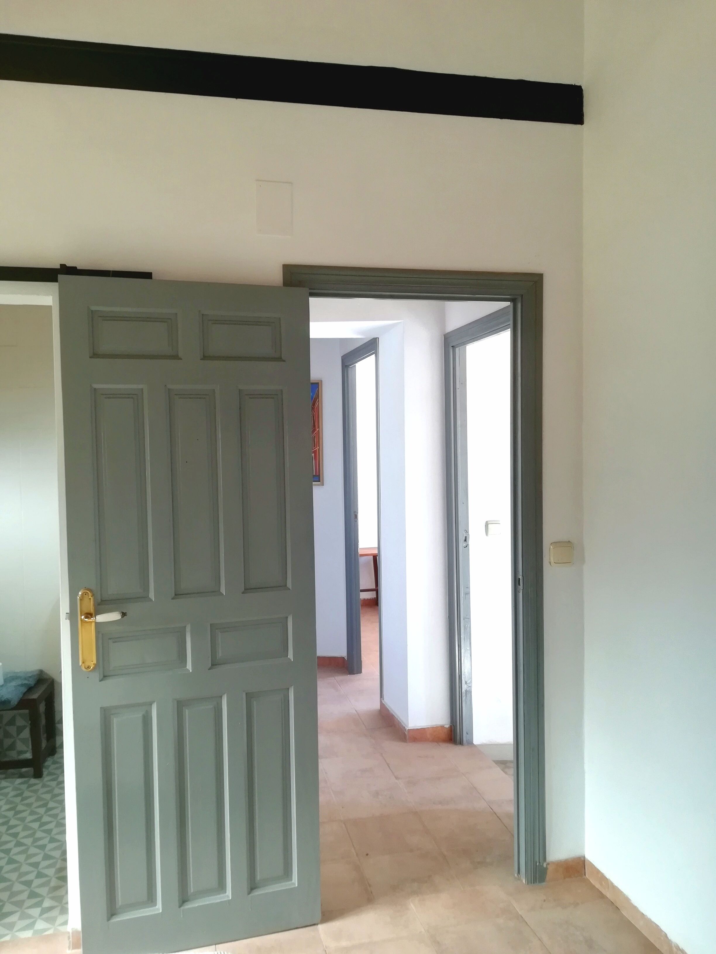 Una puerta abierta que da a un pasillo con suelo de baldosas e interruptor de luz en la pared.