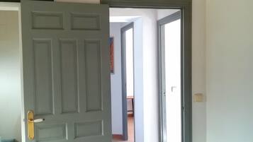 Una puerta abierta que da a un pasillo con suelo de baldosas e interruptor de luz en la pared.