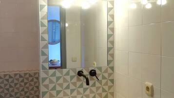 Ein Badezimmer mit einem weißen Waschbecken, zwei schwarzen Wasserhähnen, einem Spiegel und einem geometrischen Fliesenmuster an den Wänden.