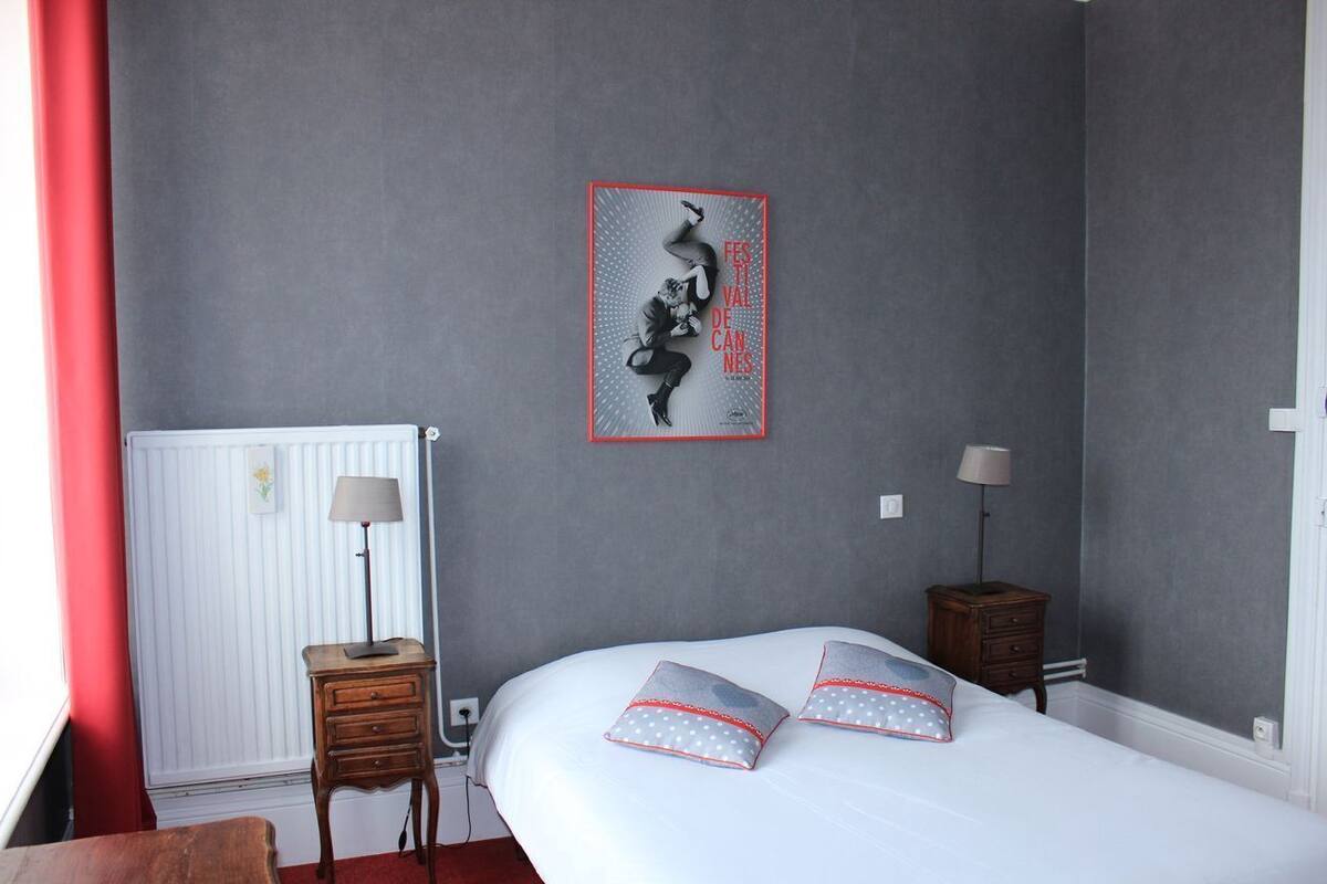 A bedroom with a bed, two bedside tables, a radiator, and a wall-mounted artwork.