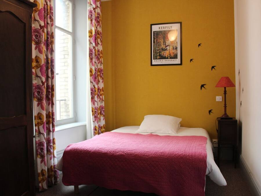 A room with a bed, a window with curtains, a wall-mounted lamp, and a framed picture.