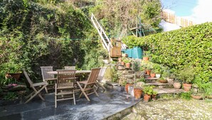 A patio with a table and chairs, surrounded by potted plants and a stone wall. - Widgeons Keel (Falmouth)