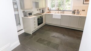 A modern kitchen with white cabinets, a built-in oven, a microwave, and a sink. - Widgeons Keel (Falmouth)