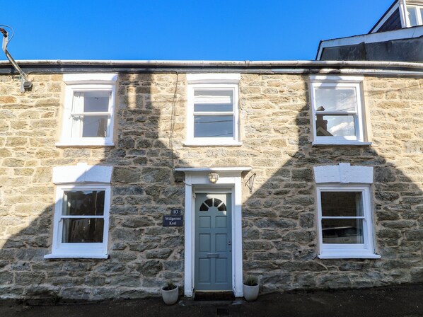 A stone building with a central door, two windows on each side, and a small sign above the door. - Widgeons Keel (Falmouth)
