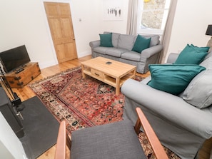 A living room with a grey sofa, a wooden coffee table, a patterned rug, a television on a wooden cabinet, and a door.
