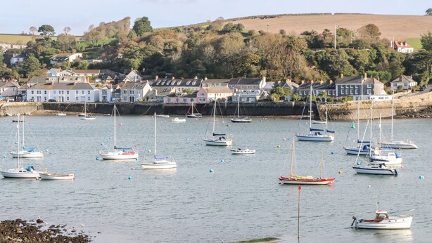 A harbor with multiple boats and a coastal town in the background. - Widgeons Keel (Falmouth)