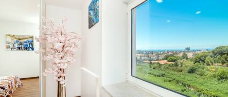 A room with a large window offering a view of a cityscape and greenery.
