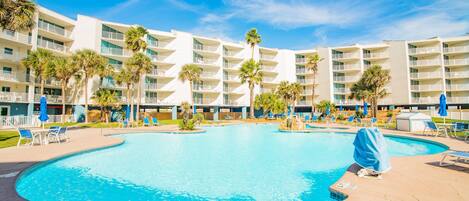 A large swimming pool surrounded by a hotel with multiple balconies and palm trees.