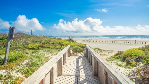 A wooden boardwalk leading to a beach with a clear sky and clouds. - Sandcastle Condominium Unit 128 (Port Aransas)