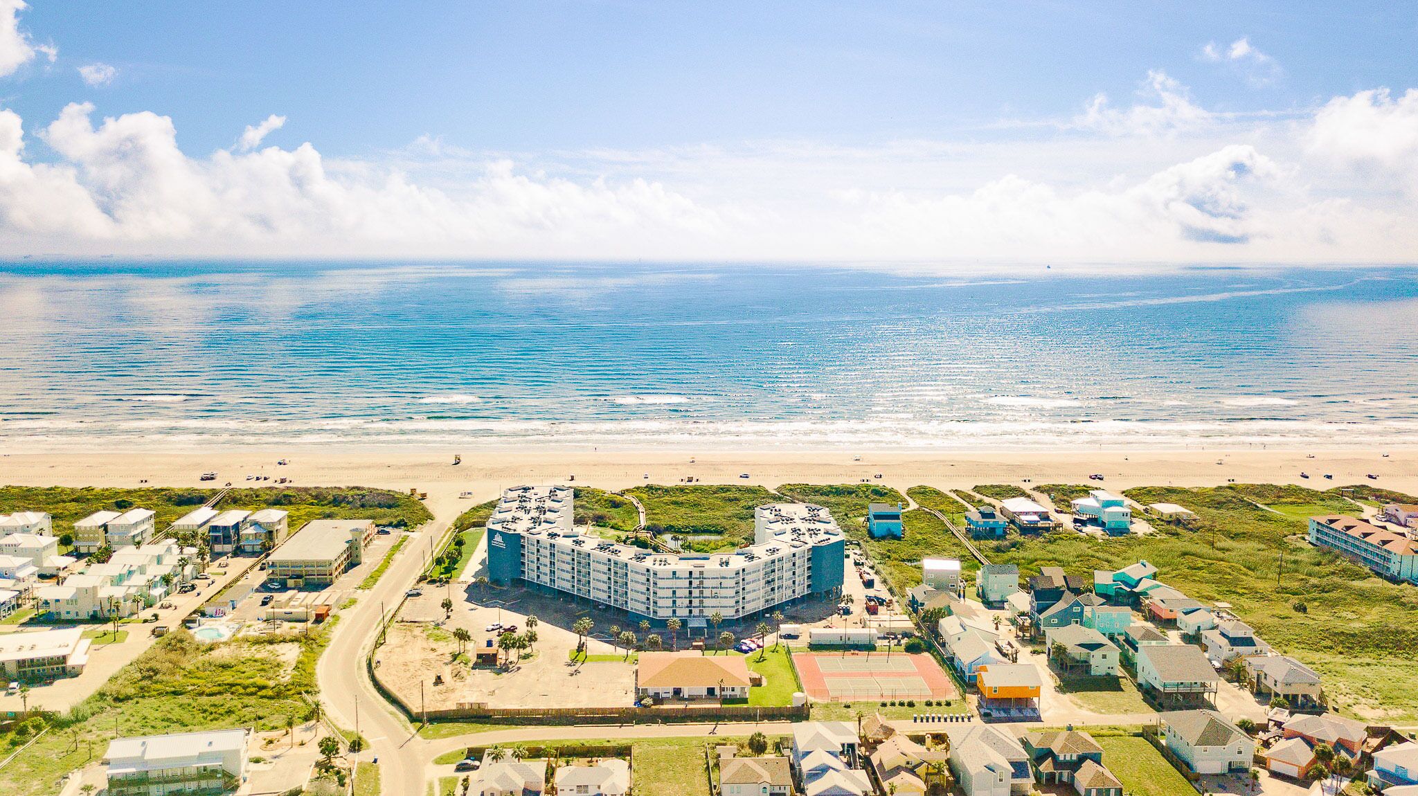 Une vue aérienne d’un hôtel situé sur la côte, avec un bâtiment principal entouré de constructions plus petites, une plage et une vue dégagée sur l’océan.