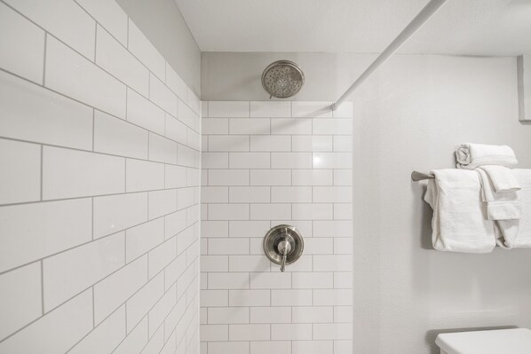A bathroom with white tiled walls, a showerhead, and a toilet with a towel rack. - Sandcastle Condominium Unit 128 (Port Aransas)