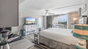 A hotel room with a bed, a desk, a television, a balcony, and a view of the ocean. - Sandcastle Condominium Unit 128 (Port Aransas)