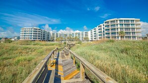 A modern hotel with multiple balconies and a wooden boardwalk leading to the entrance. - Sandcastle Condominium Unit 128 (Port Aransas)
