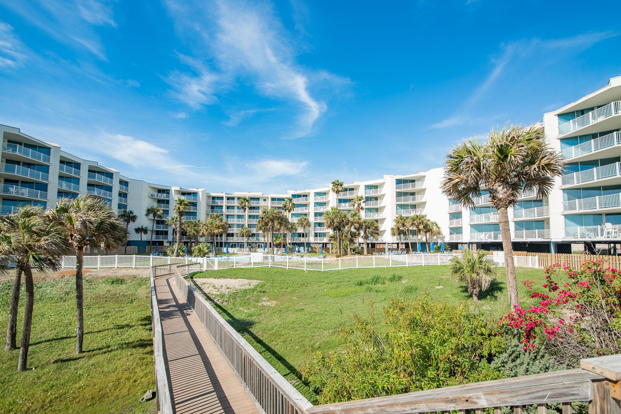 A resort with multiple-story buildings, a central pool area, and a wooden boardwalk.