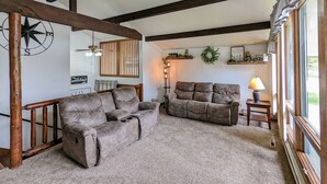 Ein gemütliches Wohnzimmer mit zwei grauen Sofas, einer Holzbalkendecke, einem an der Wand befestigten Kompass und einem Fenster mit Vorhängen.