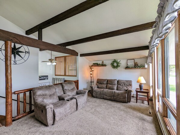 A cozy living room with two sofas, a wooden ceiling, a wall-mounted compass, and a window with curtains.