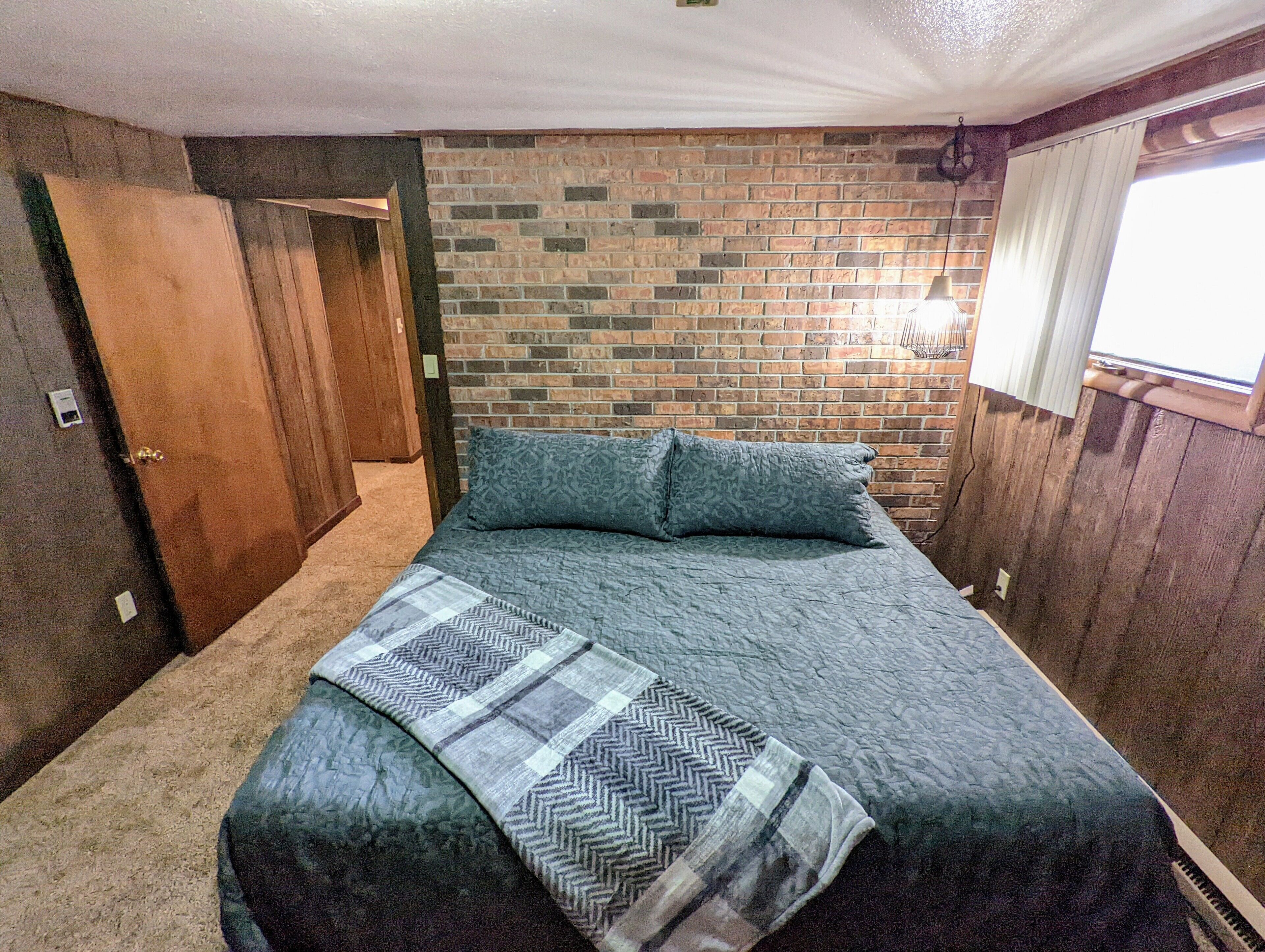 Un dormitorio con pared de ladrillo, una puerta de madera y una ventana con persianas.