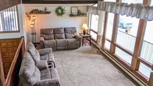 Ein Wohnzimmer mit einer Eckcouch, einer Lampe und großen Fenstern.