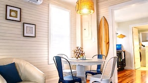 A cozy living room with a wooden ceiling, a dining area with a round table and chairs, and a surfboard on the wall. - The Loft at Oakland Beach 
Ask About Off-season Discounts 
5 min from Airport. (Warwick)