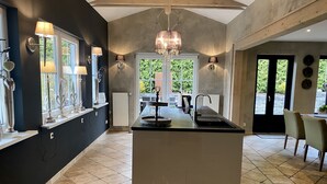 Een moderne keuken met een centraal eiland, hangende verlichting en uitzicht op de omgeving.