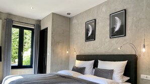 Een moderne slaapkamer met een groot bed, een nachtkastje, een wandlamp en twee ingelijste veren aan de muur.