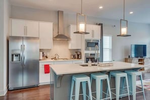 A modern kitchen with white cabinets, stainless steel appliances, a central island with bar stools, and pendant lighting.