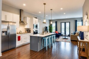 A modern kitchen with stainless steel appliances, a central island with bar stools, and a dining area with a sofa and table.