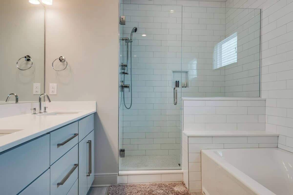 A modern bathroom with a glass-enclosed shower, a white bathtub, and a vanity with a mirror and sink.