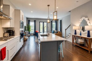 A modern kitchen with a central island, wooden flooring, and a dining area with a staircase.